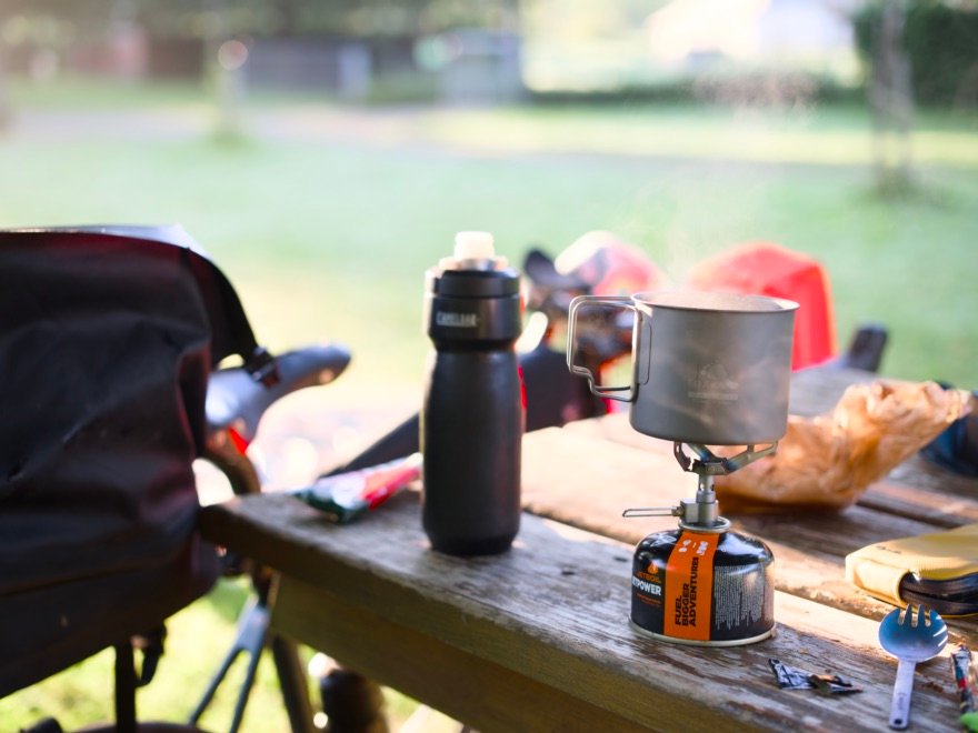 Top 5 des meilleures sporks pour le bivouac et le bikepacking 16 Matériel de bivouac à vélo avec réchaud, popote, gourde et spork posés sur une table en bois