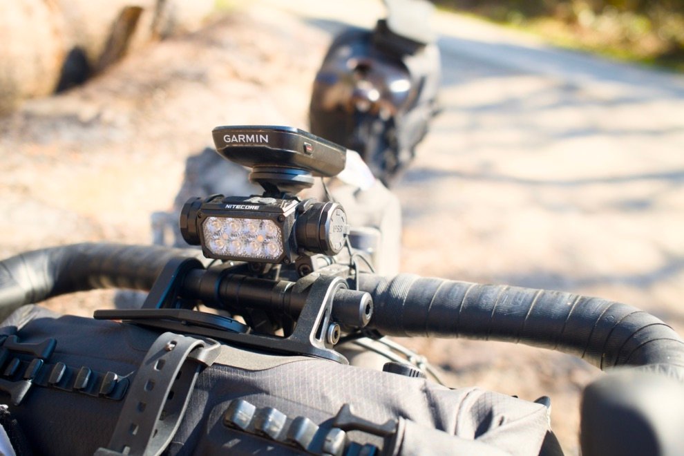 Lampe frontale Nitecore HC65 UHE fixée sur le guidon d’un vélo de bikepacking avec support Garmin