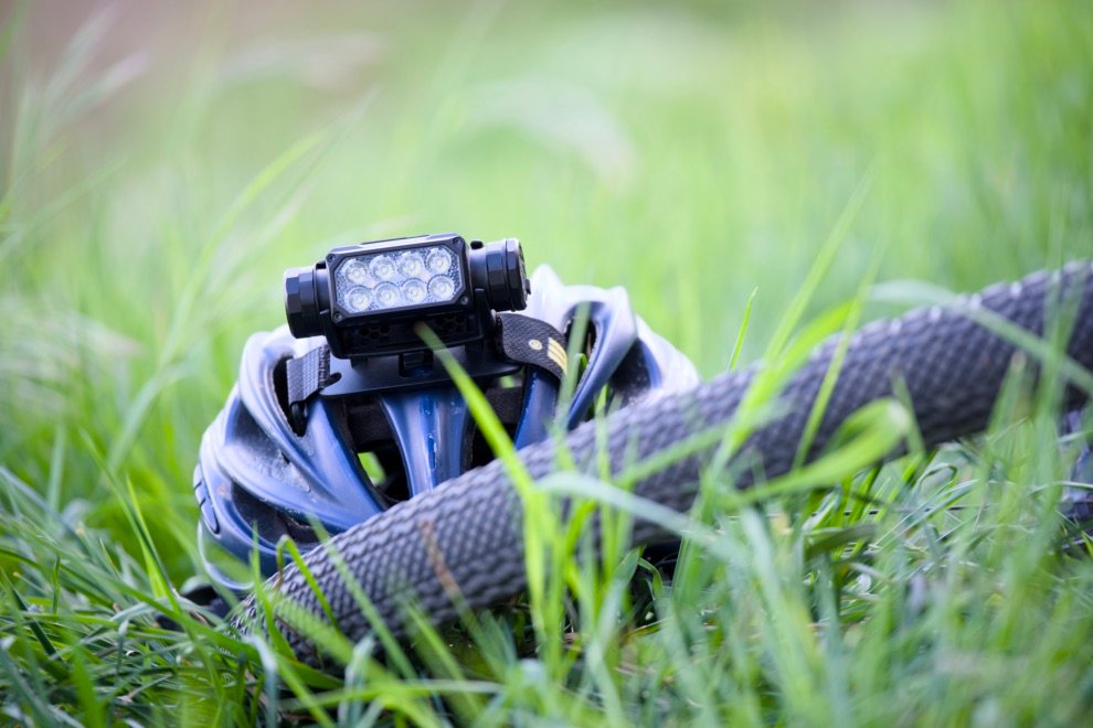 Test & Avis Nitecore HC65 UHE : La lampe frontale ultime pour le bikepacking ? 10 Lampe frontale Nitecore HC65 UHE montée sur un casque de vélo avec fixation scratch, posée dans l’herbe