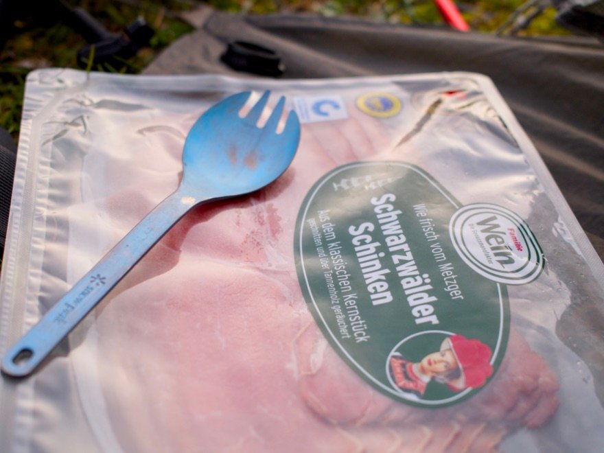 Top 5 des meilleures sporks pour le bivouac et le bikepacking 15 Spork en titane Light My Fire posée sur un sachet de jambon de Forêt-Noire pendant un bivouac