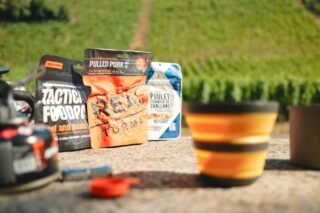 Sachets de repas lyophilisés posés en extérieur avec vue sur des vignes, prêts pour un bivouac en bikepacking.