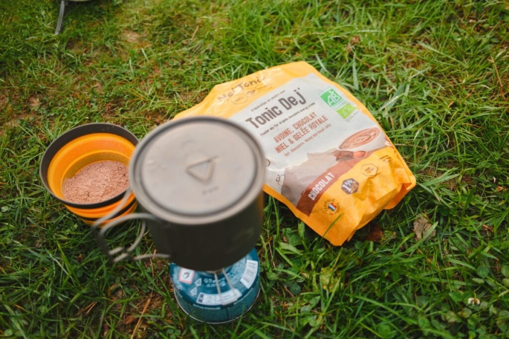 Préparation d’un petit déjeuner chaud en bikepacking avec la poudre Tonic Dej Meltonic au chocolat, sur un réchaud de camping