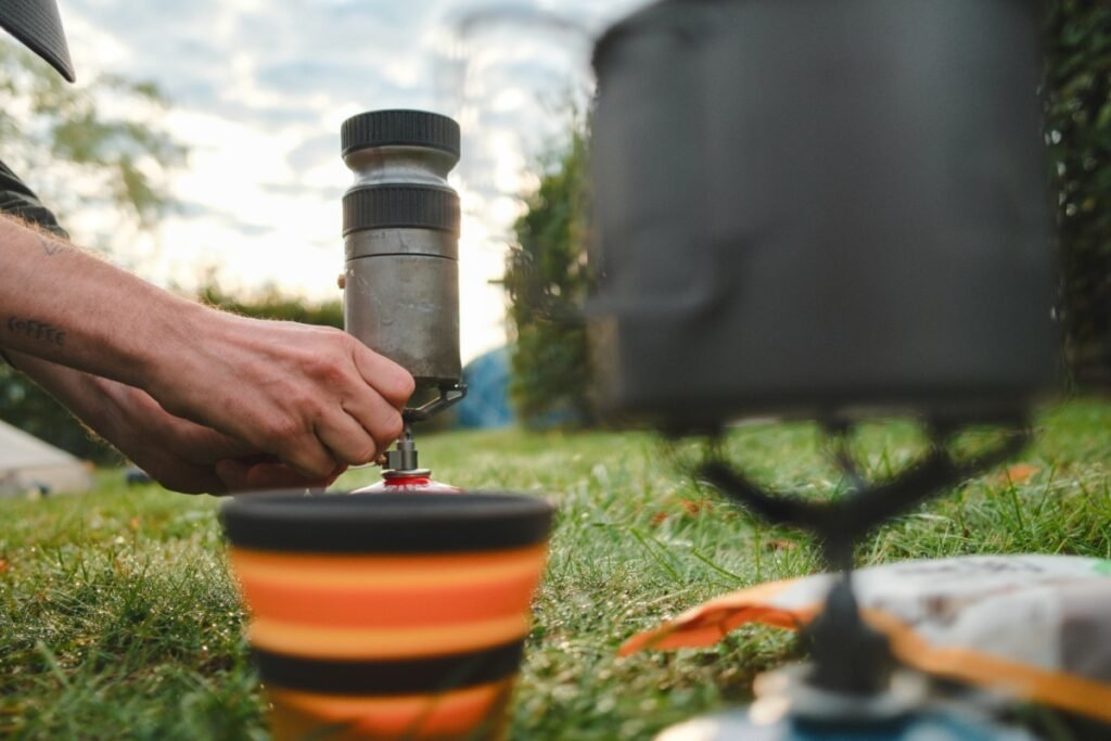 Préparation d’un café en bikepacking avec un réchaud à gaz au petit matin, vue sur les mains en train d’allumer le brûleur