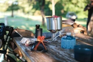 Le petit déjeuner en bikepacking 4 Préparation d’un petit déjeuner en bikepacking sur une table de pique-nique avec réchaud à gaz, popote en inox et sachet de muesli