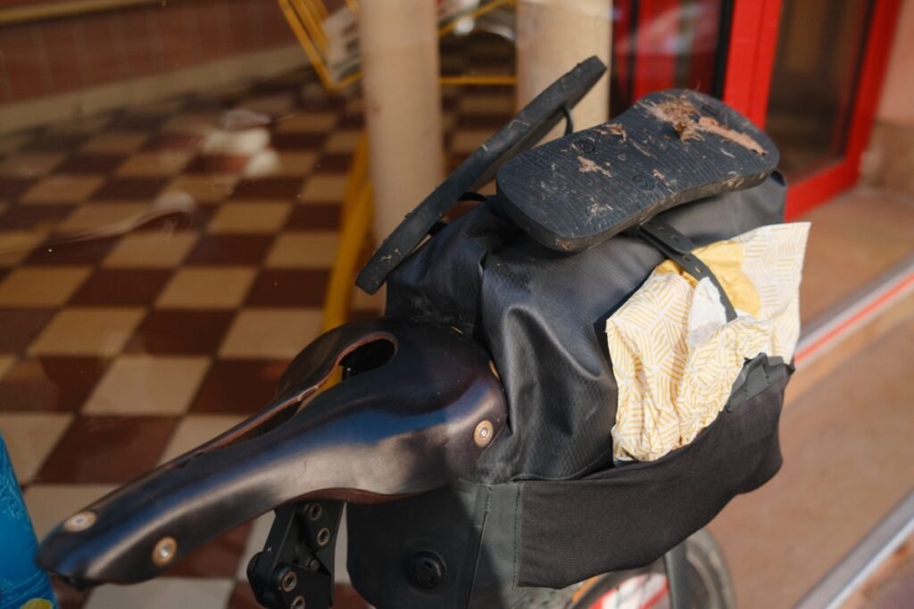 Sacoche de selle de vélo de bikepacking contenant des viennoiseries achetées à la boulangerie, avec une selle en cuir et une sandale posée dessus