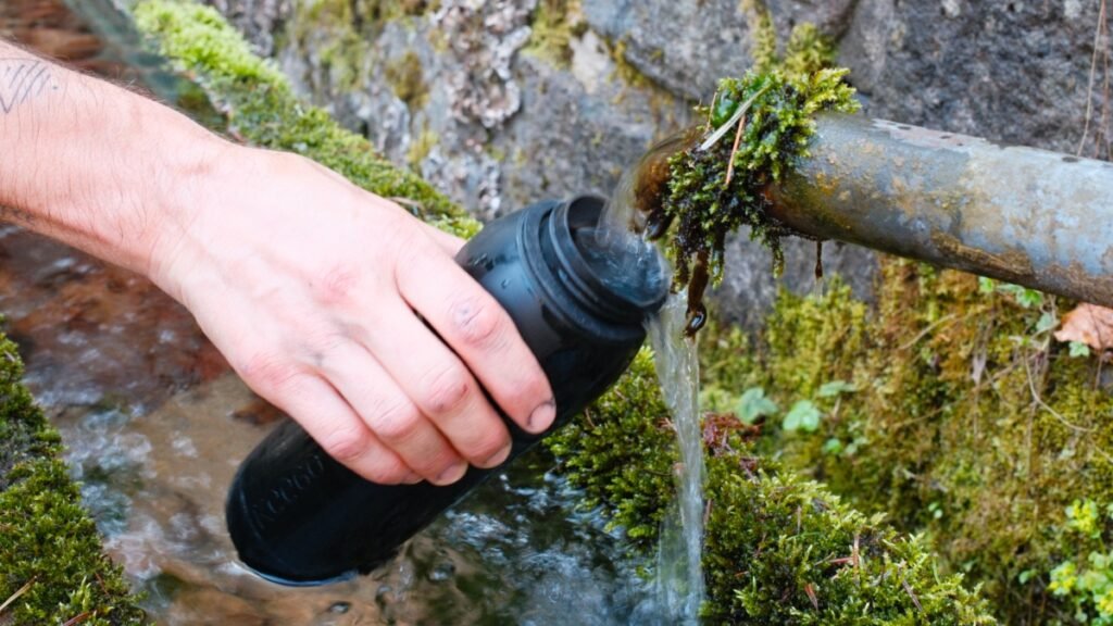 Que manger en bikepacking ? Conseils et matériel pour bien s’alimenter à vélo 8 Cycliste remplissant une gourde d’eau fraîche à une source pendant un voyage en bikepacking