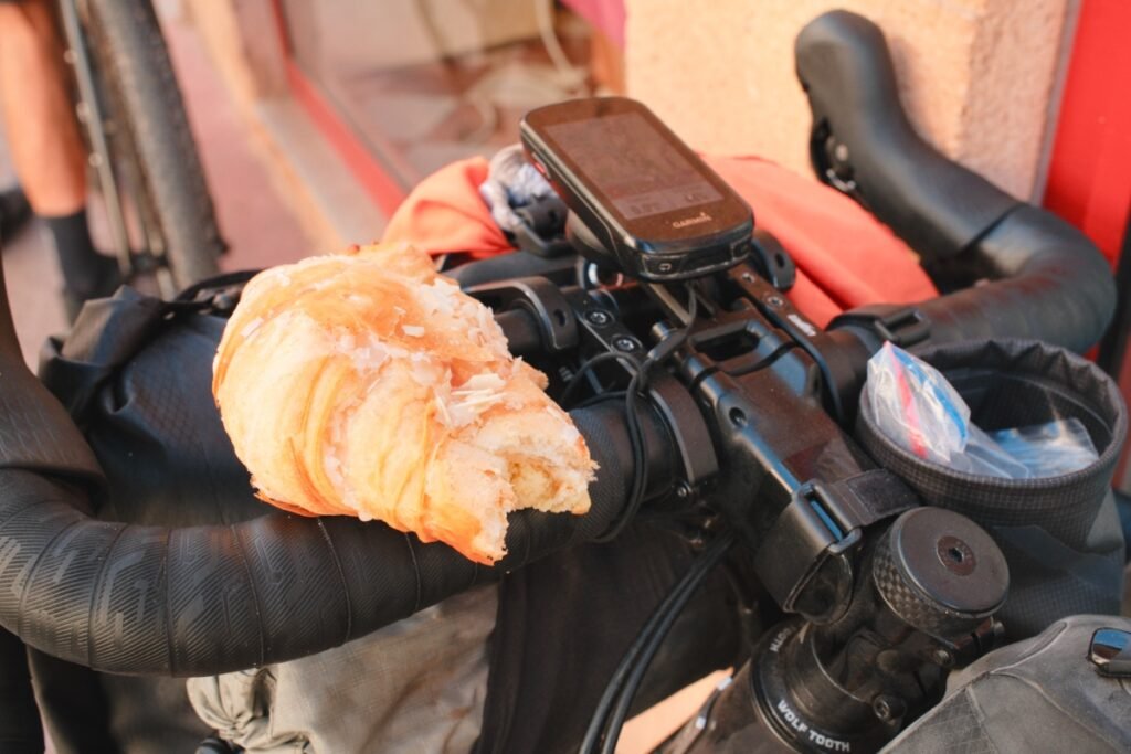 Que manger en bikepacking ? Conseils et matériel pour bien s’alimenter à vélo 5 Croissant posé sur un vélo de bikepacking pour le petit-déjeuner avant une journée de voyage à vélo