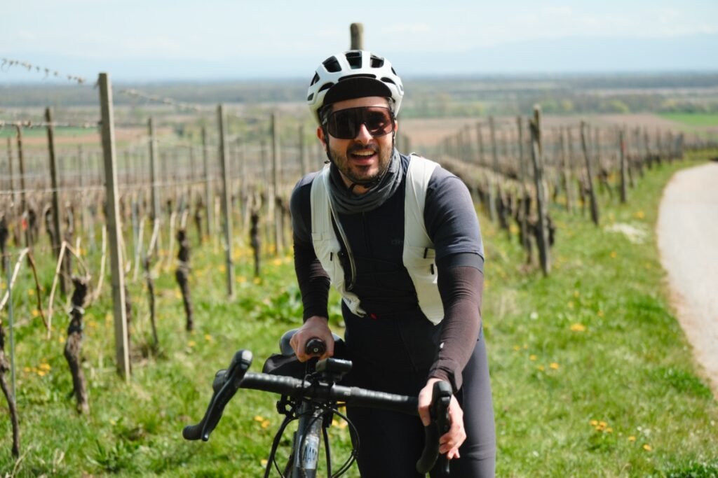 Cycliste souriant sur son gravel portant le gilet d'hydratation Cyclite Hydration Vest /01 dans les vignes