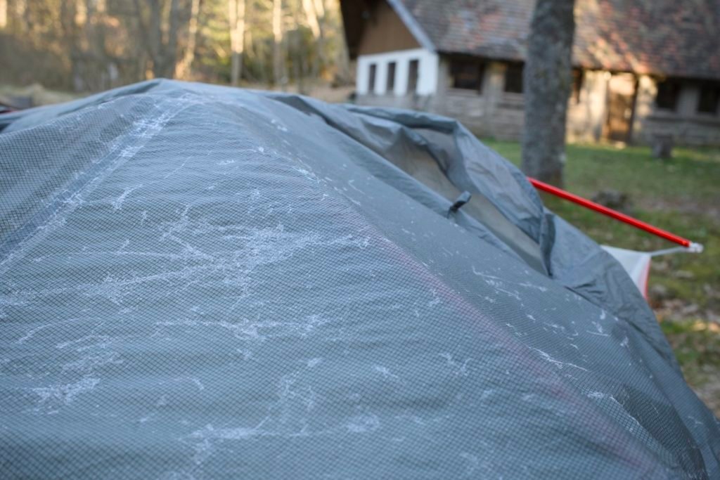 Traversée de la Forêt-Noire en gravel : 544 km en 5 jours, du pneu éclaté à la tente gelée 7 Toile de tente grise recouverte de givre au petit matin, montée sur une pelouse devant un bâtiment en bois et en pierre, lors d'un bivouac en Forêt-Noire