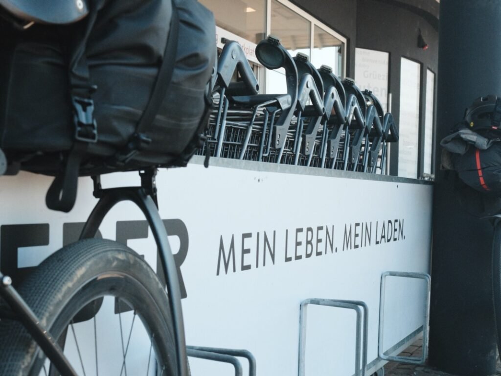 Traversée de la Forêt-Noire en gravel : 544 km en 5 jours, du pneu éclaté à la tente gelée 2 Vélo gravel chargé d'une sacoche de selle, garé devant un supermarché allemand portant l'inscription « Mein Leben. Mein Laden. »