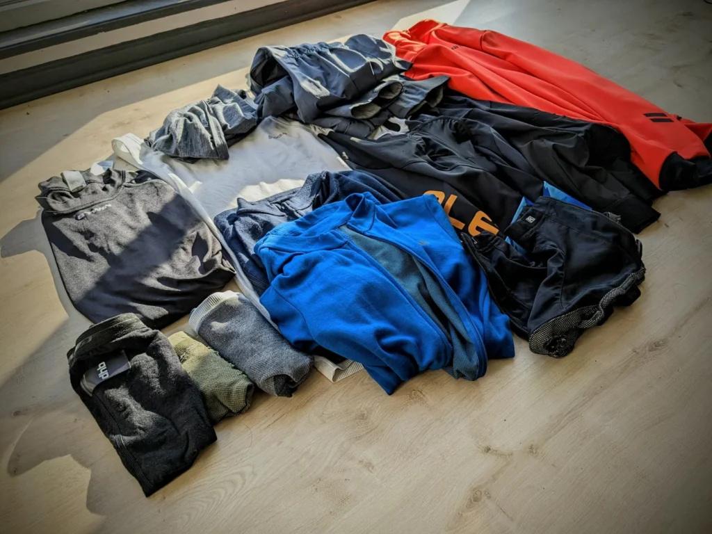 Quels vêtements emporter en bikepacking ? 5 Vêtements de bikepacking étalés sur un parquet avant le départ : maillots, cuissards, sous-couches en mérinos, chaussettes et vestes de vélo.