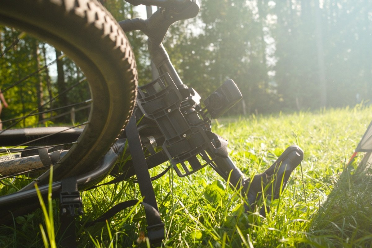 Vélo de bikepacking couché dans l'herbe au bivouac, à contre-jour, avec le compteur GPS fixé à l'avant du cintre et le support de sacoche de guidon.