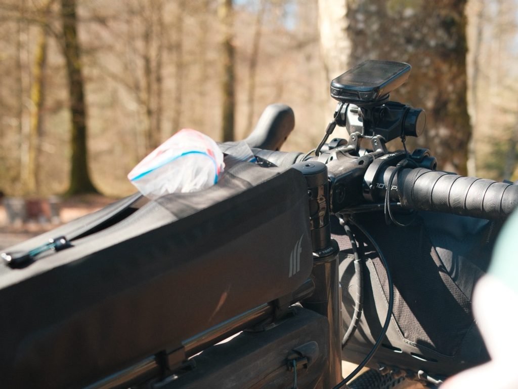 Compteur GPS fixé sur un support déporté au-dessus de la potence, avec une lampe en dessous, sur un vélo de bikepacking équipé d'une sacoche de guidon et d'une sacoche top tube.
