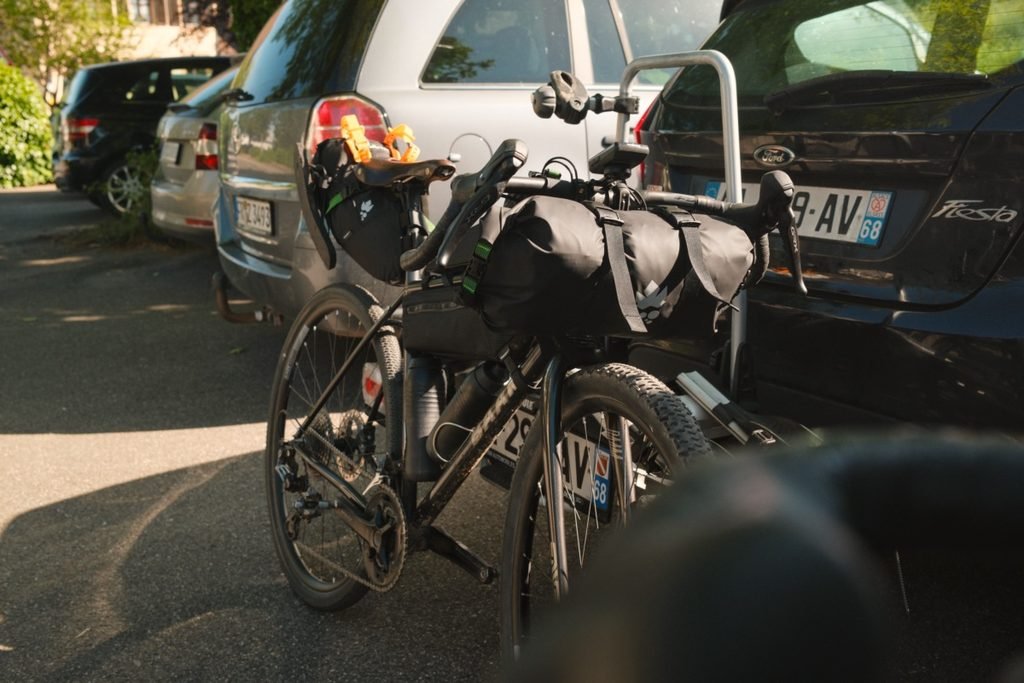 Vélo gravel chargé pour un voyage en bikepacking, avec sacoche de guidon et sacoche de selle, installé sur un porte-vélo à l'arrière d'une voiture avant le départ.